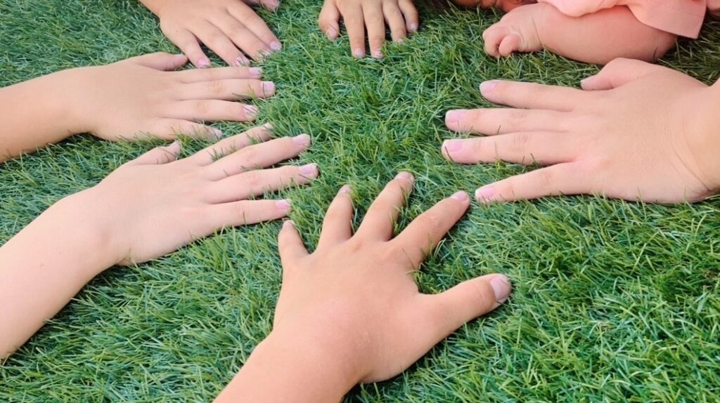 子供たち7人が芝生の上で手を合わせている様子